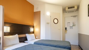 Habitación de hotel con dos camas, cabecera de madera, aire acondicionado de pared y una puerta con espejo y documentos.