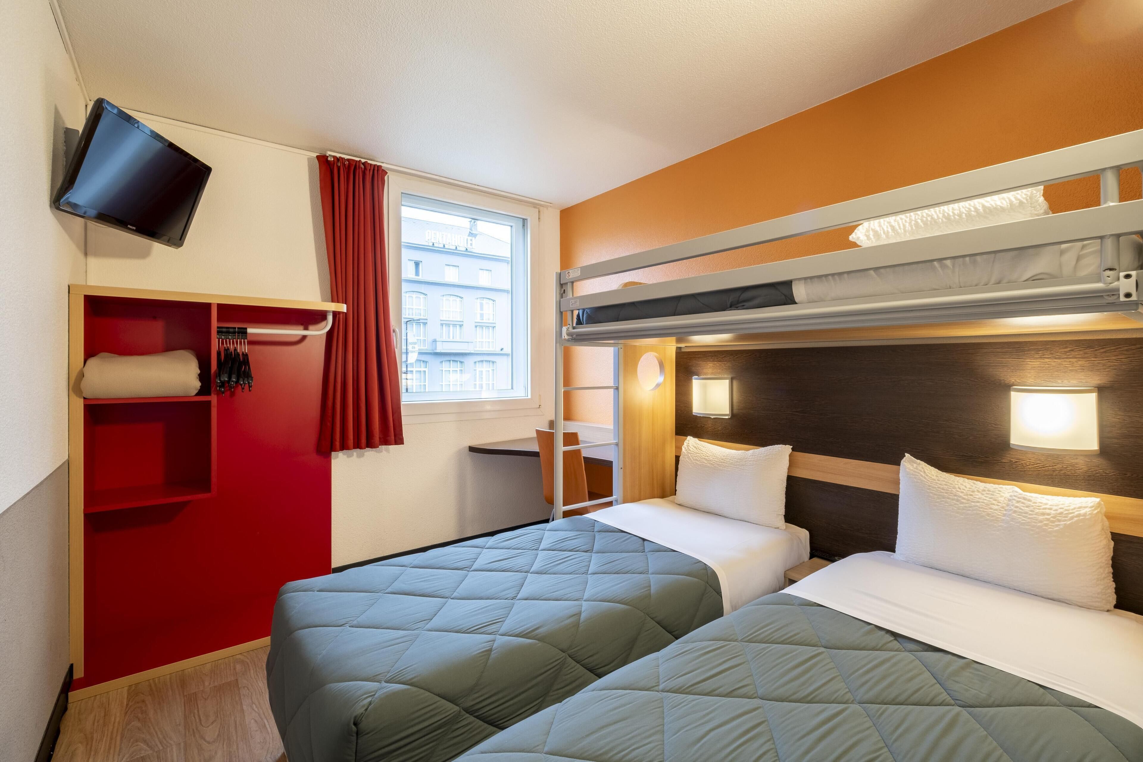 Habitación de hotel con dos camas, un televisor montado en la pared y una ventana con cortinas.