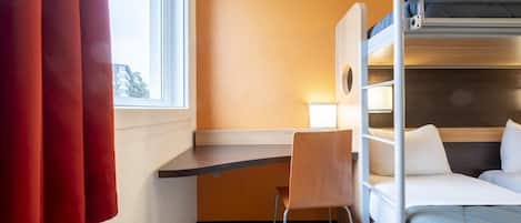 Ein Schlafraum mit Etagenbetten, einem Schreibtisch und Stuhl, einem Fenster mit Vorhängen und Blick auf Gebäude.