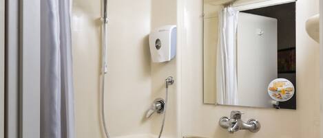 Un baño con ducha, lavamanos y espejo.