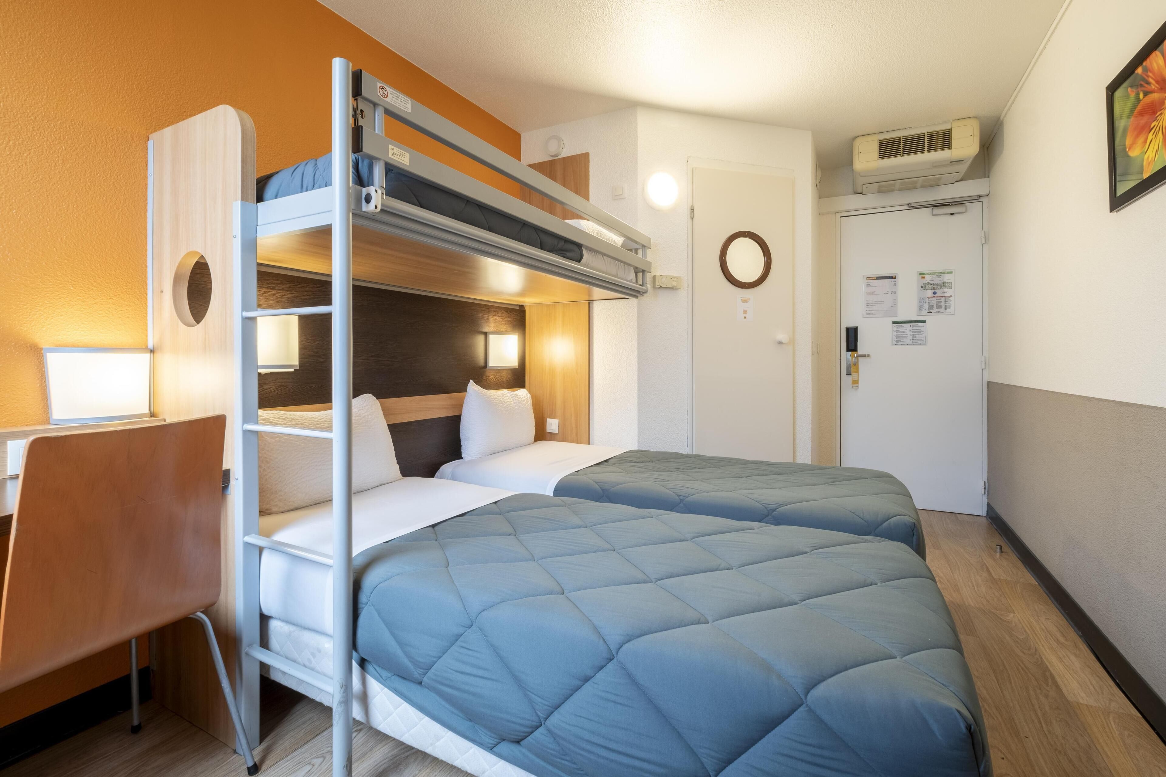 Habitación de hotel pequeña con literas, un escritorio y una silla.