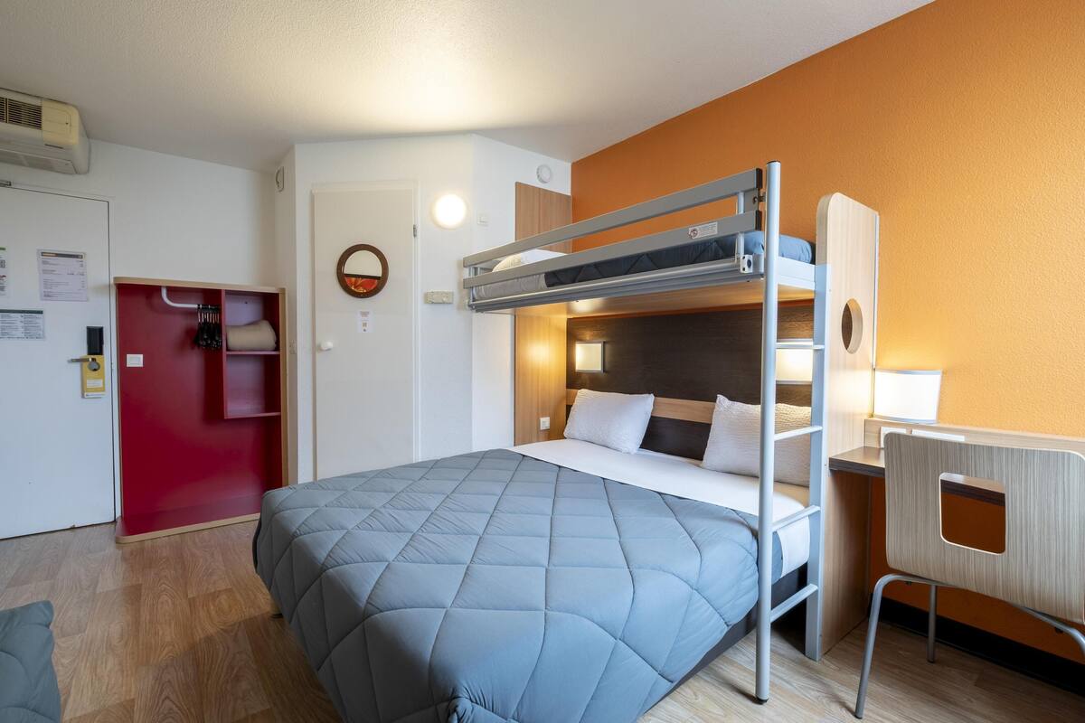Ein Stockbett mit Schreibtisch und Stuhl, ein roter Kleiderschrank und ein kleiner runder Spiegel an der Wand.