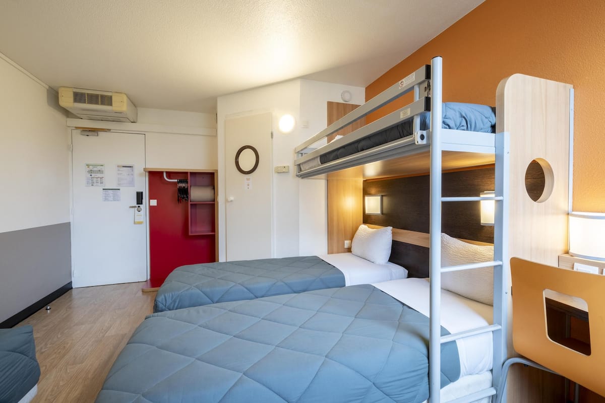 Ein kleines Hotelzimmer mit Etagenbetten, einem kleinen Schreibtisch und einer roten Tür.