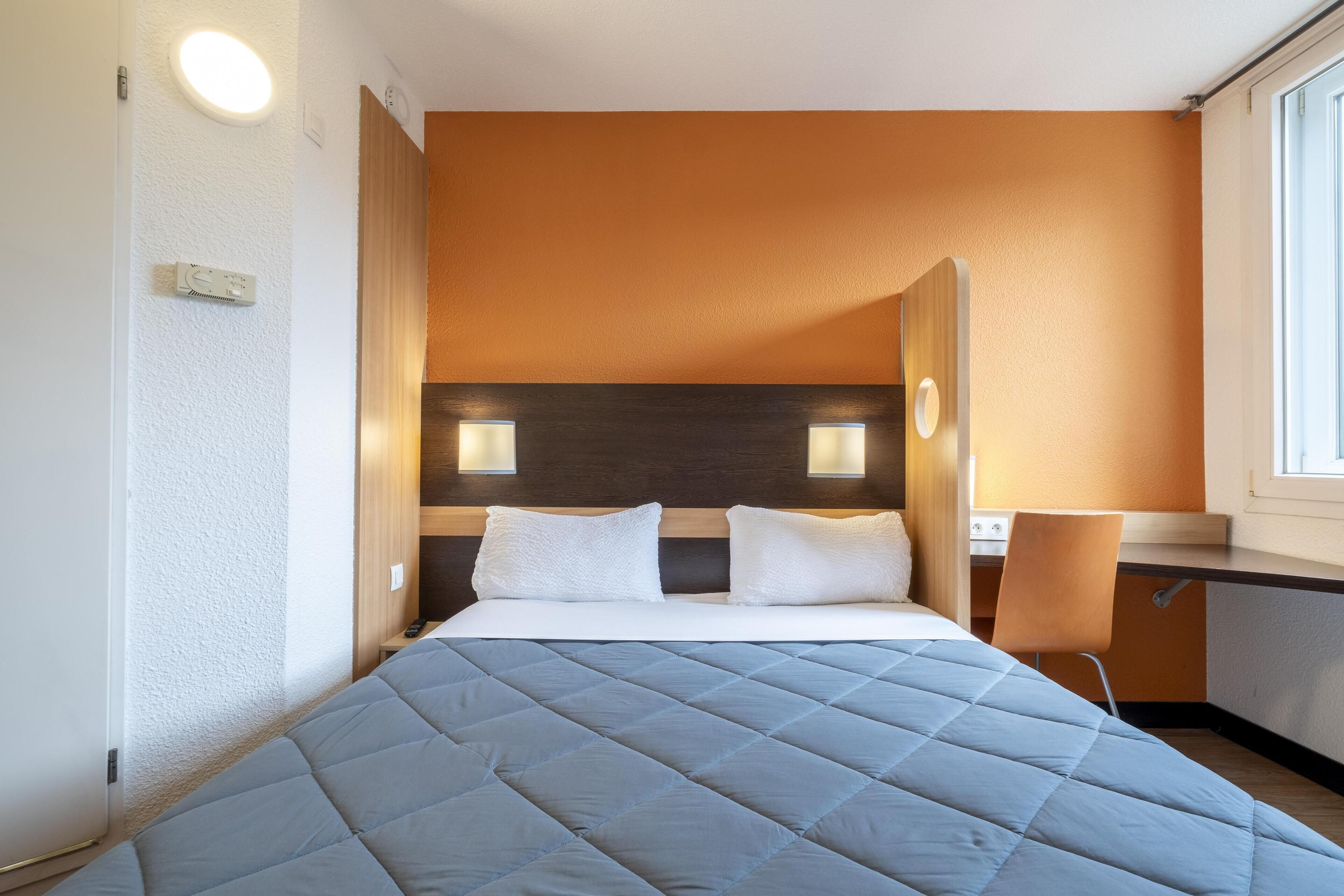 A hotel room with a bed, a desk, and a window.