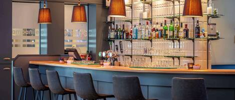 A bar area with a counter, bar stools, and shelves stocked with bottles and glasses.