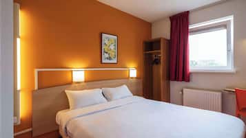 Hotelkamer met een bed, nachtlampjes, een raam met gordijnen, een radiator en een klein tafeltje.