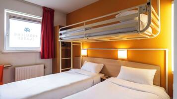 Una camera d'albergo con due letti, una finestra con tende, un termosifone e un armadio.