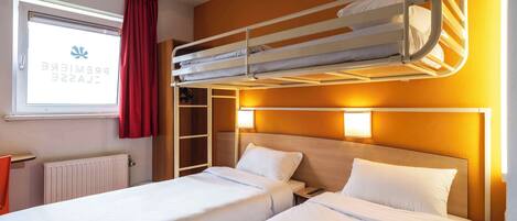 A hotel room with two beds, a window with curtains, a radiator, and a wardrobe.