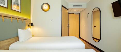 A hotel room with a bed, a wall-mounted TV, a mirror, and a door leading to another room.