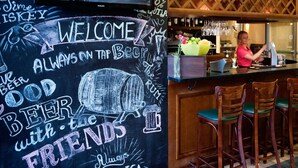 A bar area with a chalkboard sign welcoming guests and a bartender preparing drinks.