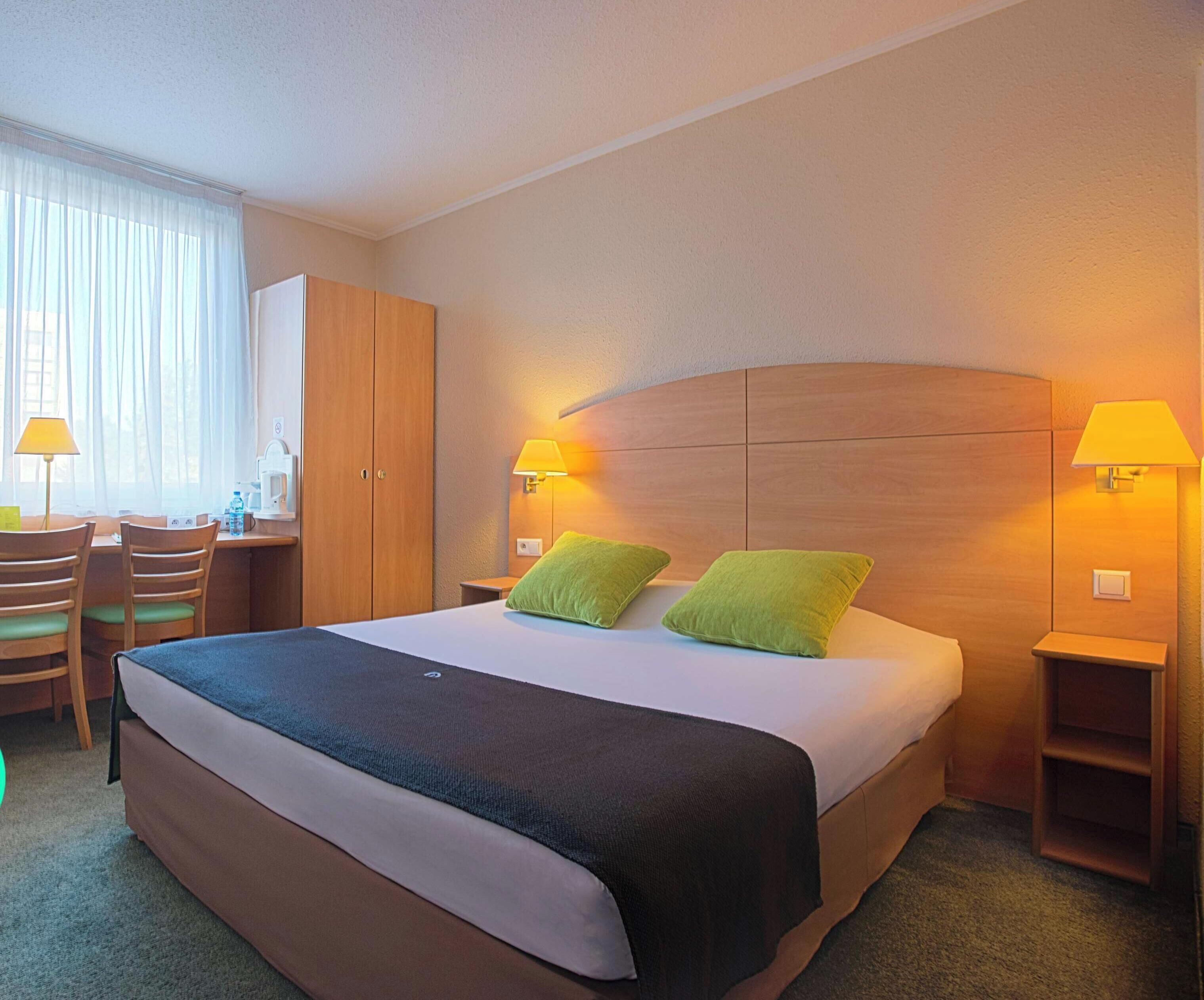 Een hotelkamer met een bed, twee bedlampen, een bureau met stoelen en een kledingkast.
