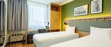 A hotel room with two beds, a desk, a chair, a trash bin, and a window with curtains.