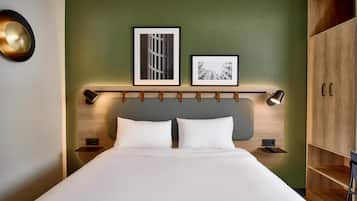 Una cama bien tendida con sábanas blancas, una pared de acento verde y dos cuadros colgados encima.
