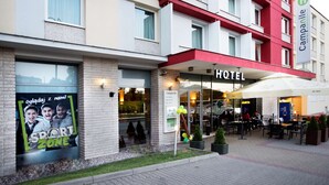 A hotel with a red and white facade, outdoor seating area, and a sign advertising a 'Sport Zone'.
