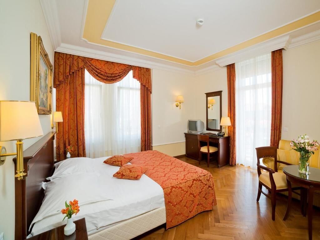 A hotel room with a large bed, a desk, a chair, a television, and a vase with flowers.