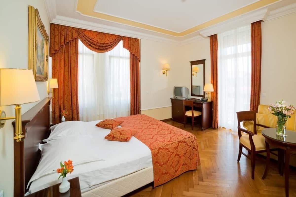 A hotel room with a large bed, a desk, a chair, a television, and a vase with flowers.