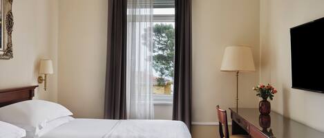 Une chambre d’hôtel avec un grand lit, un bureau avec une chaise, une télévision et une fenêtre avec des rideaux.