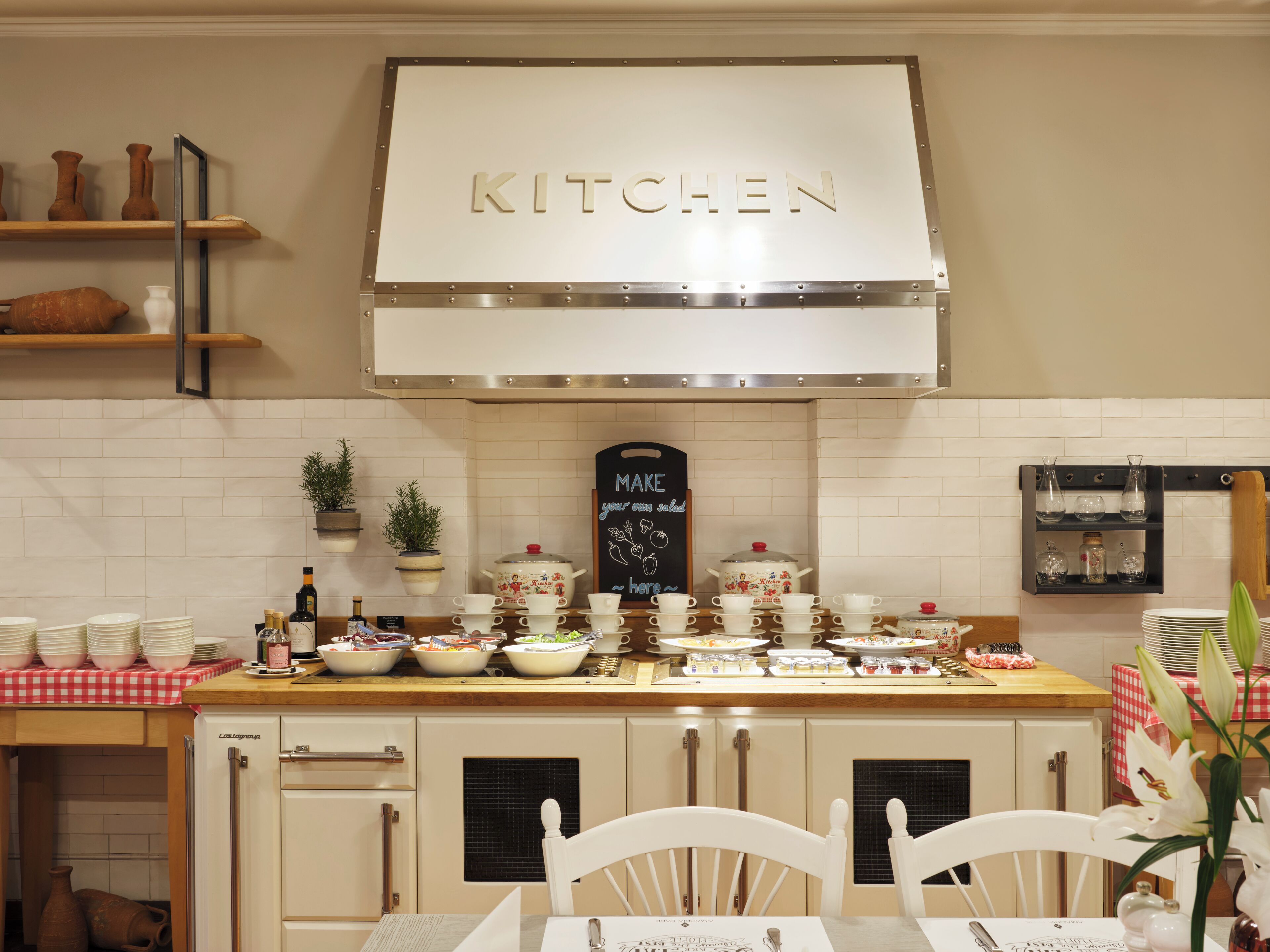 A kitchen with a 'KITCHEN' sign, white cabinets, a chalkboard menu, and various kitchenware.