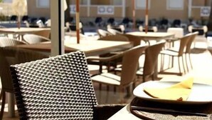 An outdoor dining area with wicker chairs and tables, a pool in the background, and a clear view of the sky.