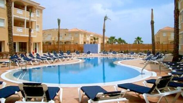 A pool area with lounge chairs and a building in the background.