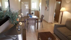 A modern living room with a sofa, a dining table with chairs, a kitchen area in the background, and a large mirror on the wall.