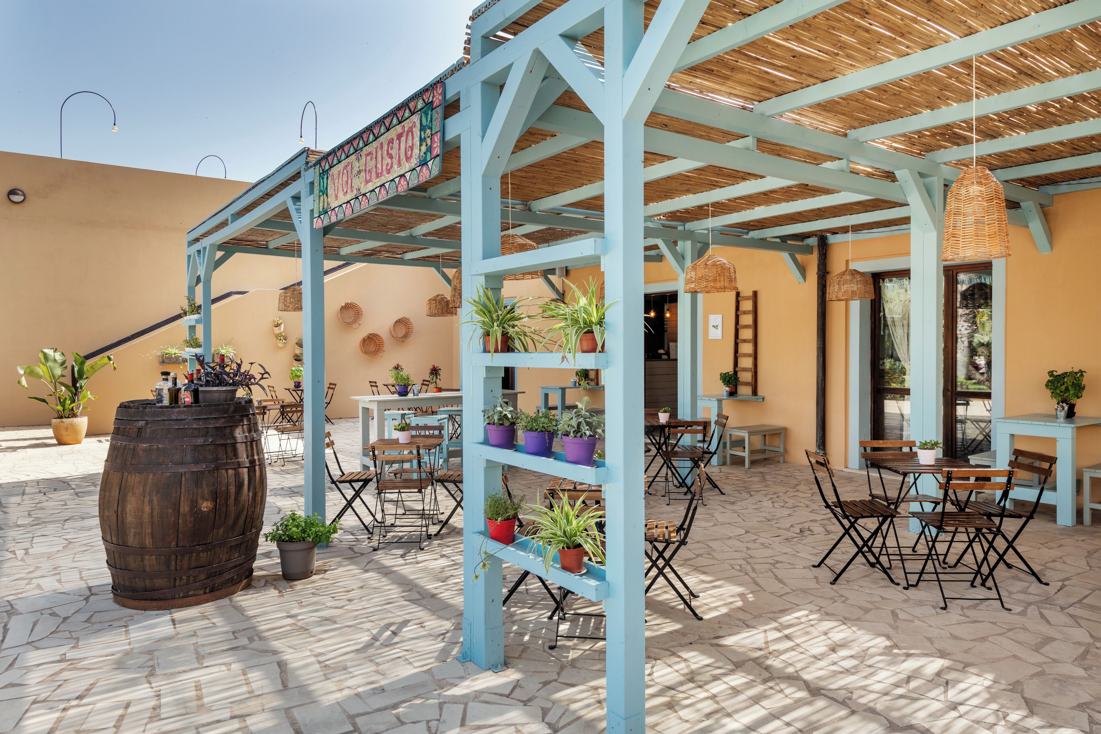 An outdoor patio area with wooden tables and chairs, potted plants, and a sign reading "Viva Vista".