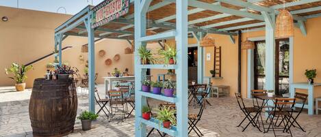 An outdoor patio area with wooden tables and chairs, potted plants, and a sign reading "Viva Vista".