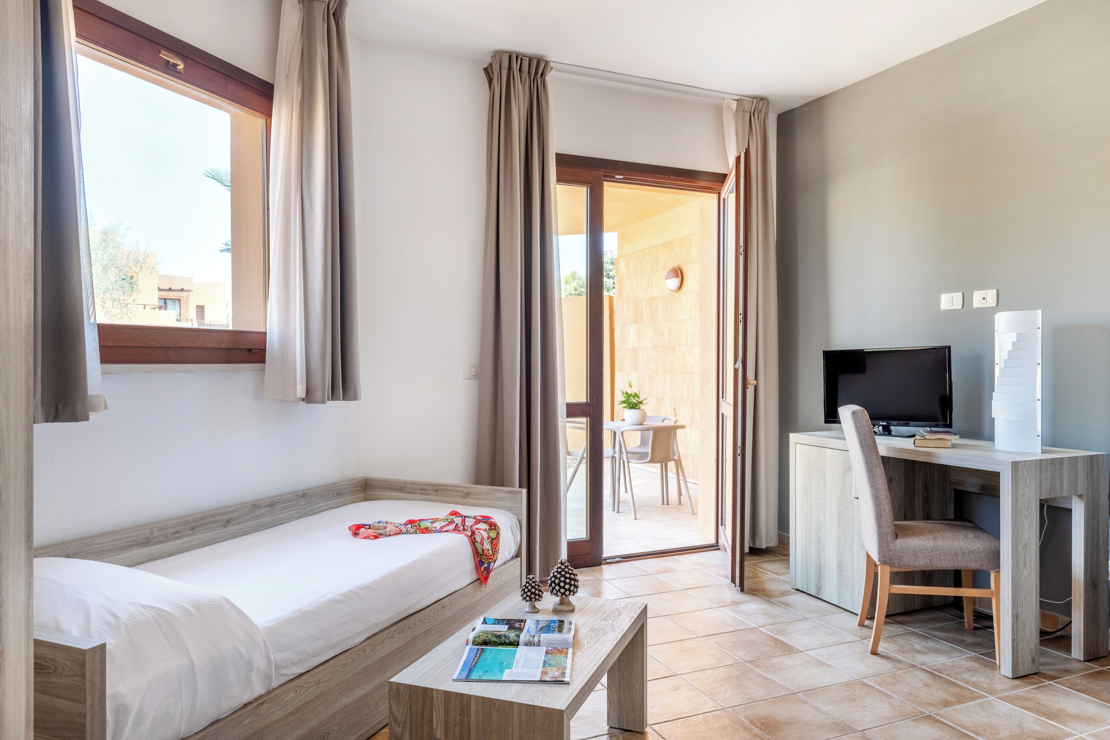 A hotel room with a bed, a desk with a computer, and a view of the outside.
