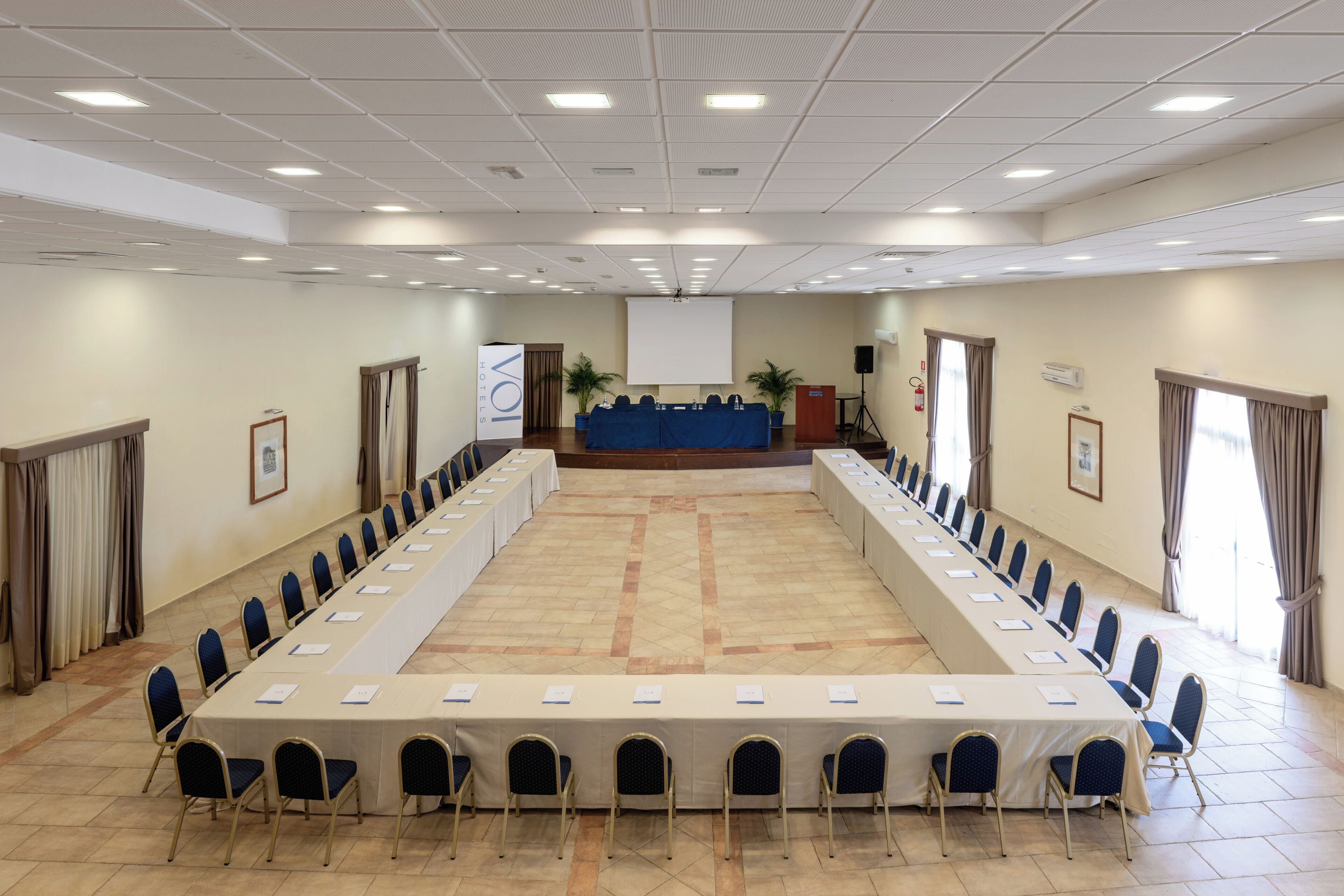 A conference room with a long table, chairs, a podium, and a projector screen.