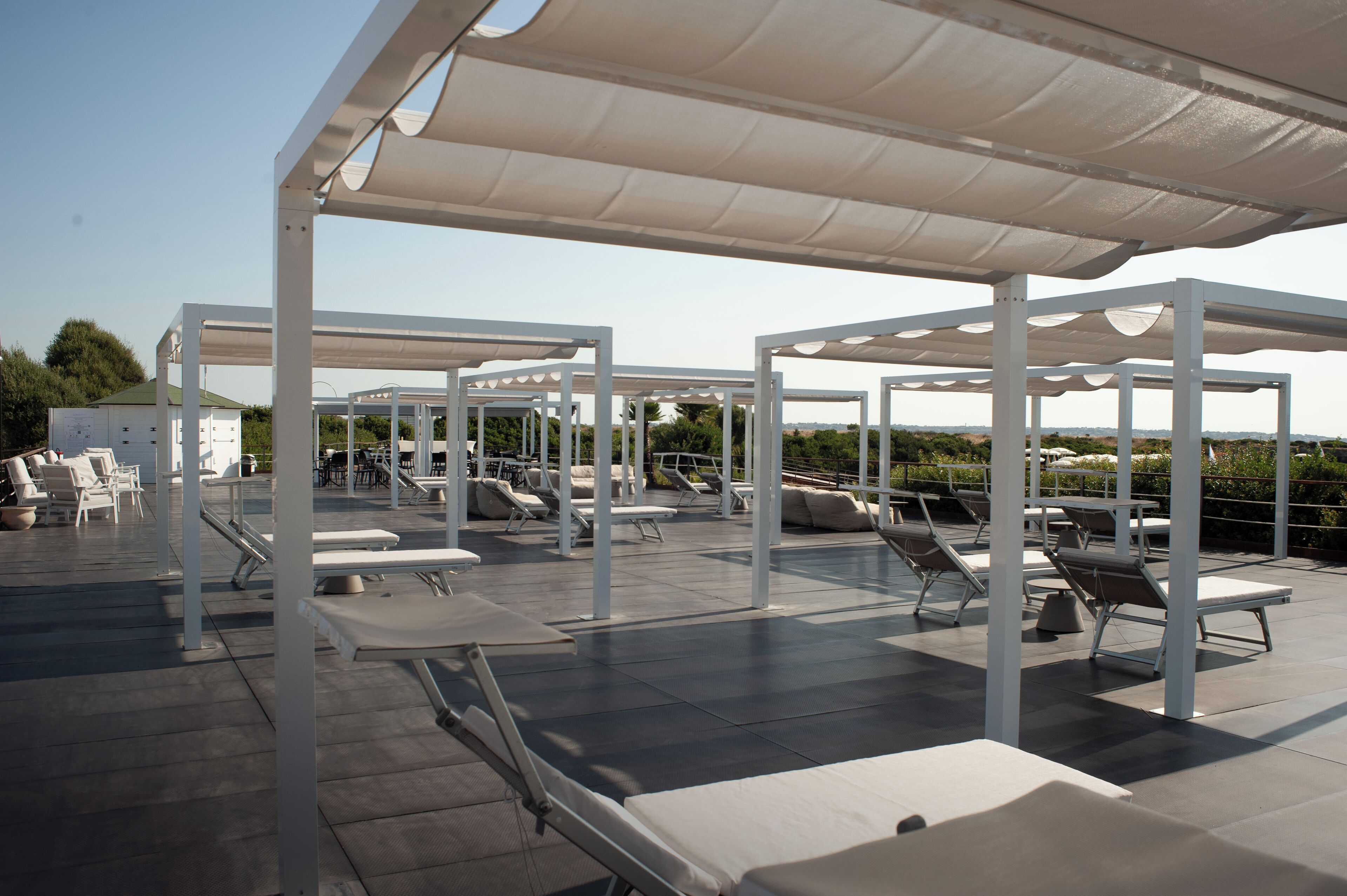 Eine Dachterrasse mit weißen Pergolen, Liegestühlen und einem Poolbereich.