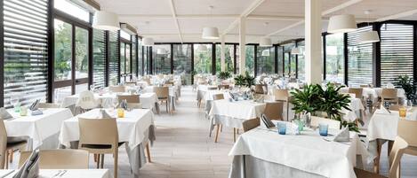 A spacious dining area with multiple tables set for dining, large windows allowing natural light, and a modern ceiling design.