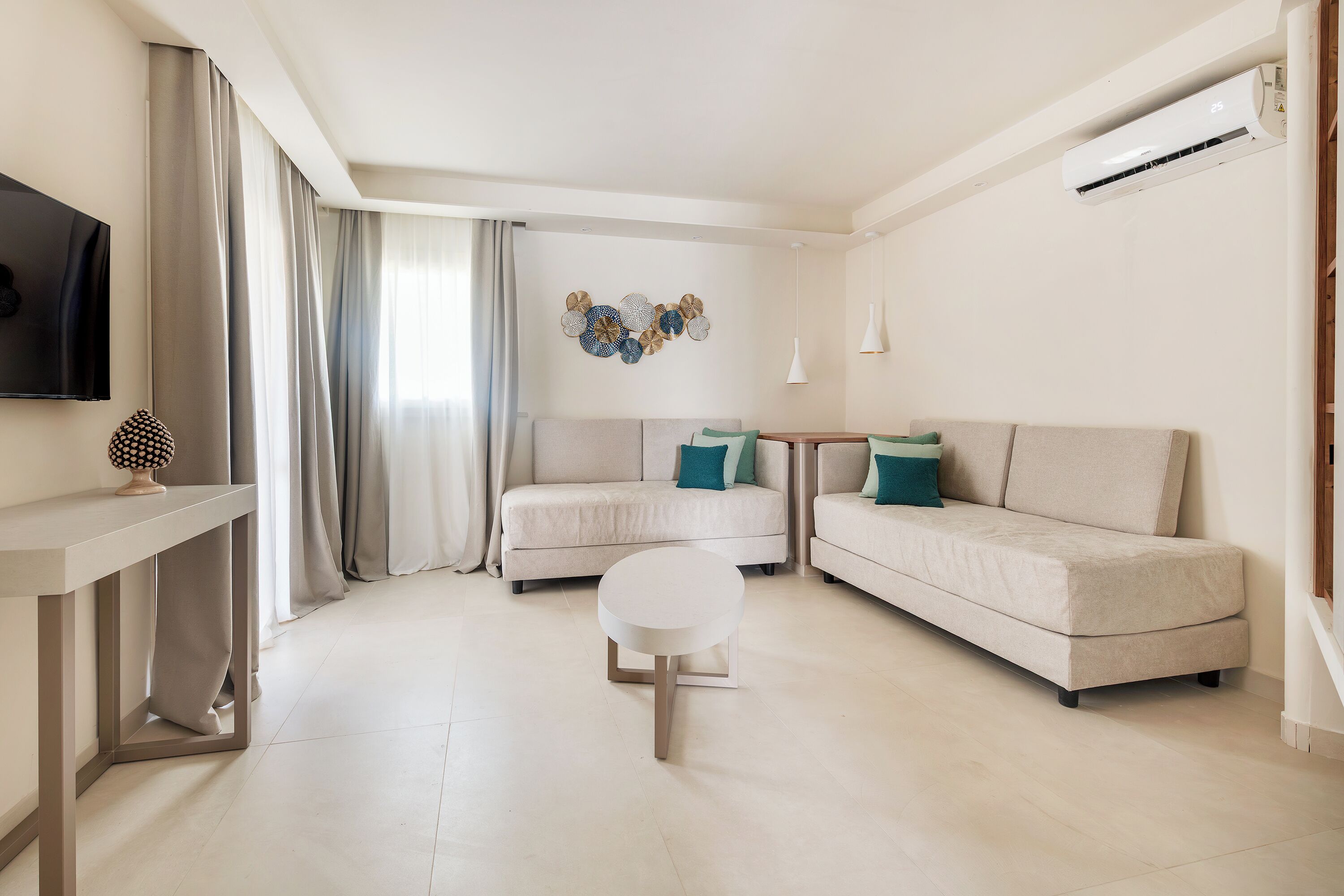 A modern living room with a sofa, a round coffee table, and a flat-screen TV mounted on the wall.