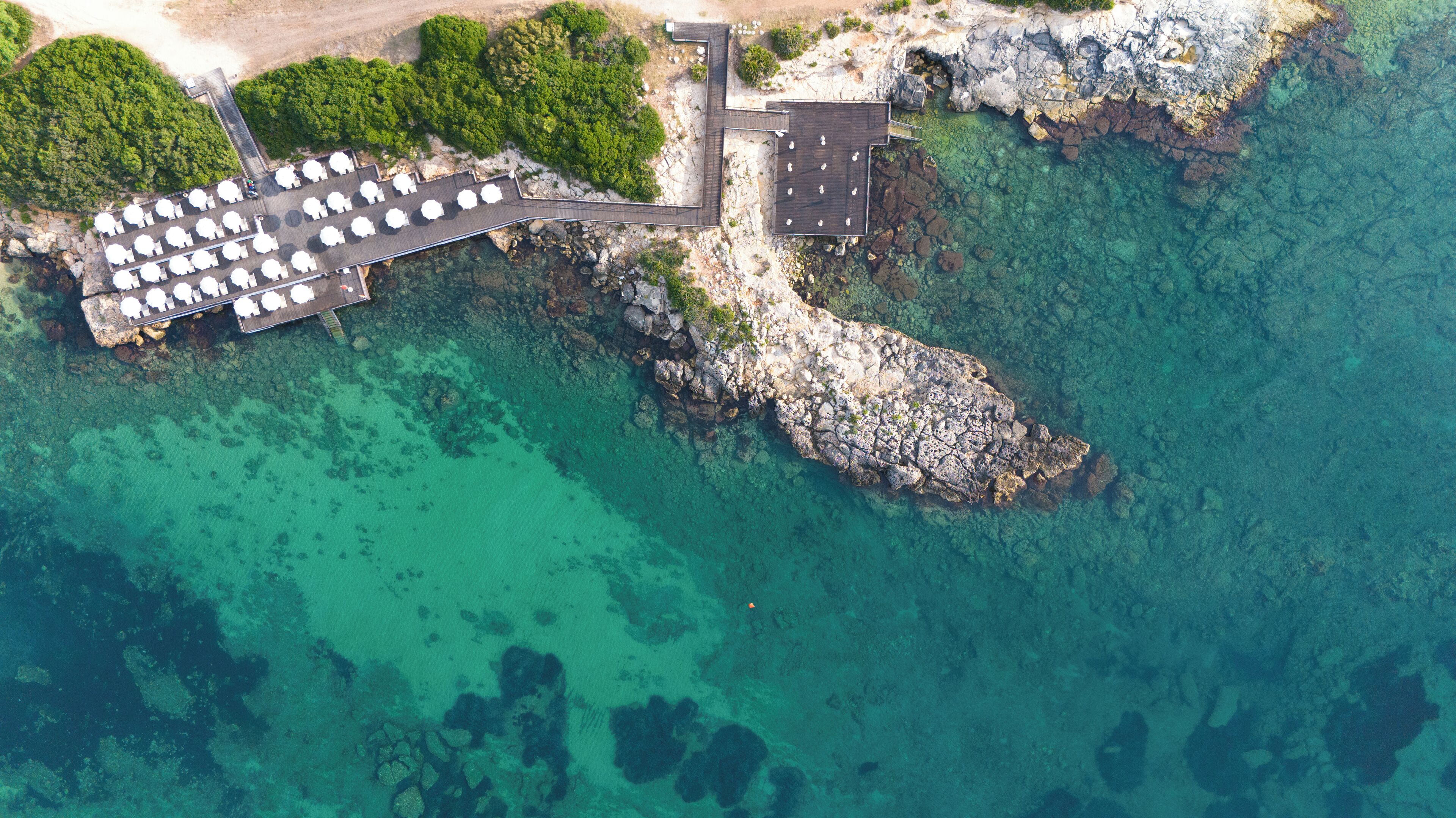 Vue aérienne d’une propriété située sur la côte, avec une jetée, un espace de stationnement et une côte rocheuse.