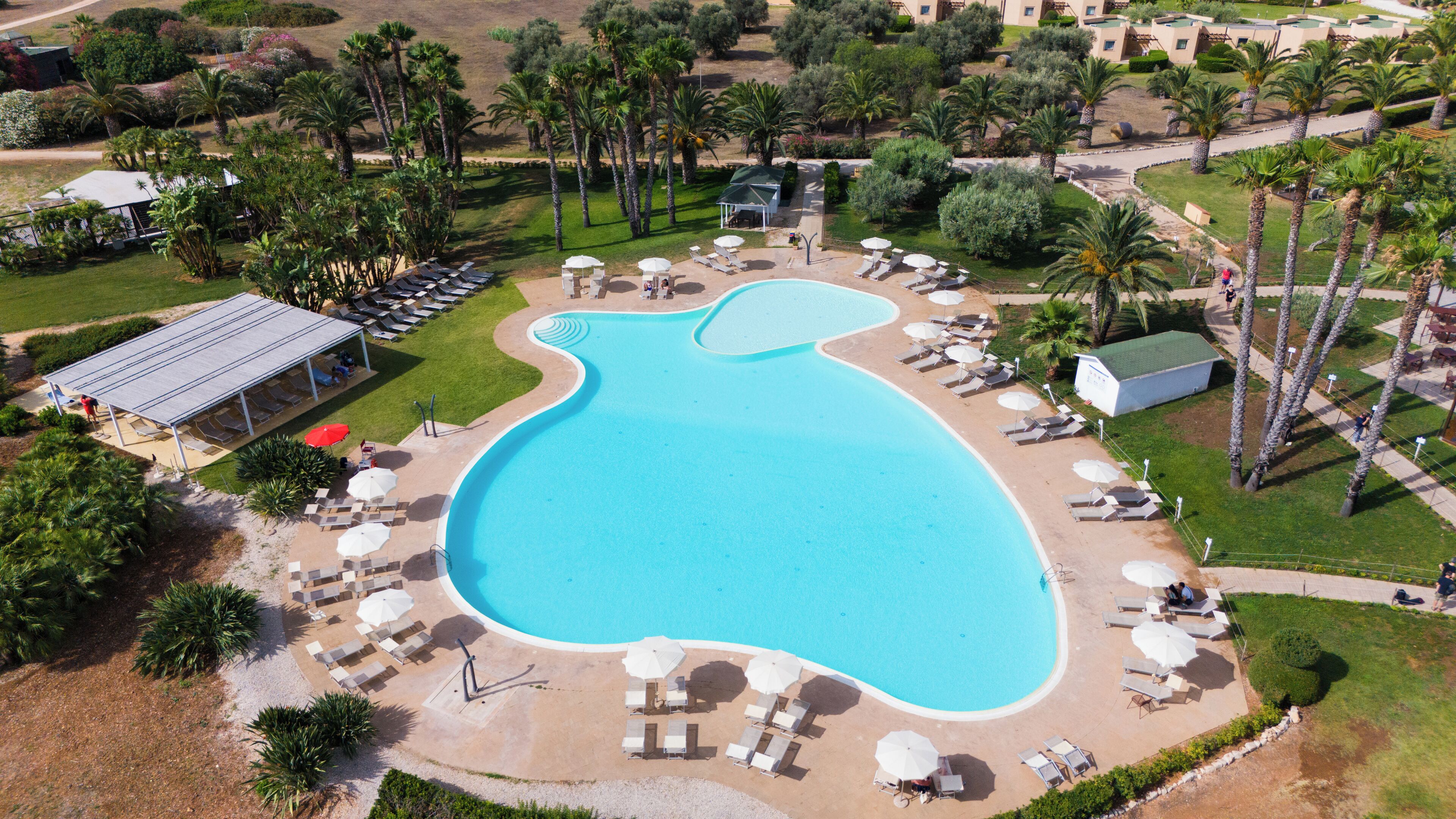 Vista aérea de un resort con una piscina grande, tumbonas y palmeras.