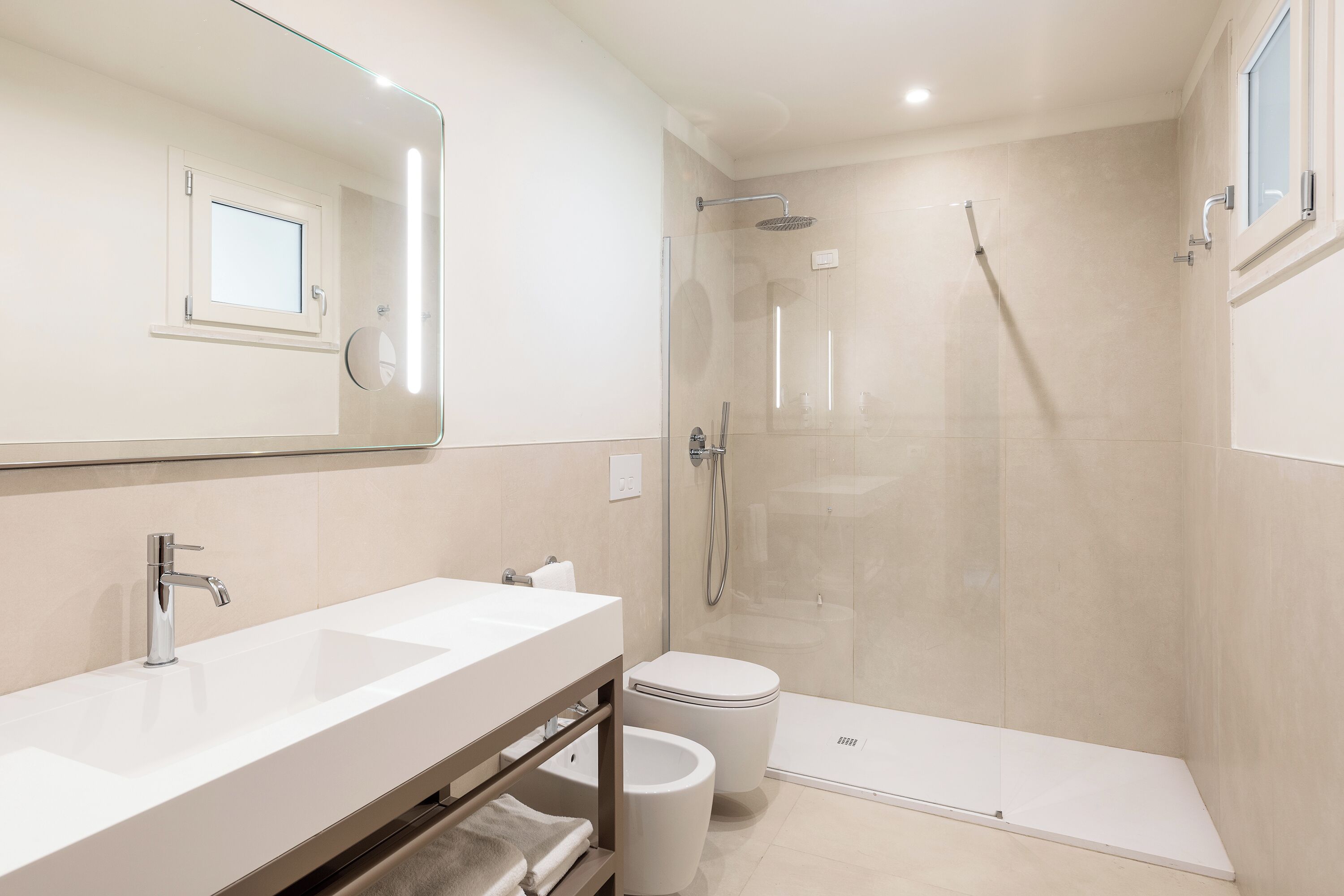A modern bathroom with a large mirror, a sink, a toilet, and a glass-enclosed shower area.