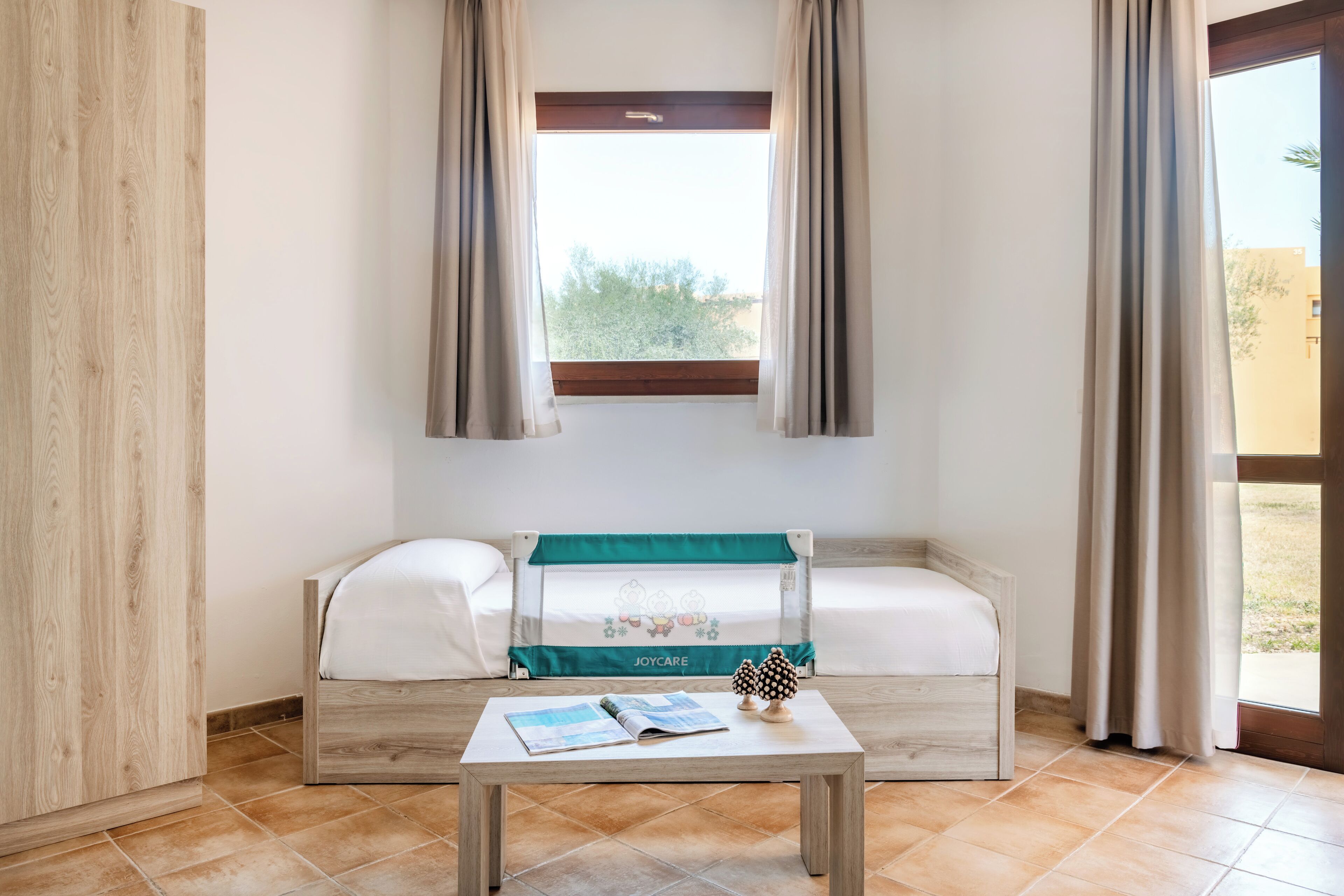 Una habitación con una cama de madera, una mesa con un libro y una ventana con cortinas.
