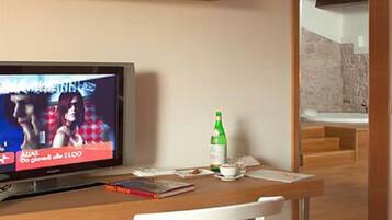 A modern hotel room with a wooden desk, a television, a white chair, and a bottle of water.