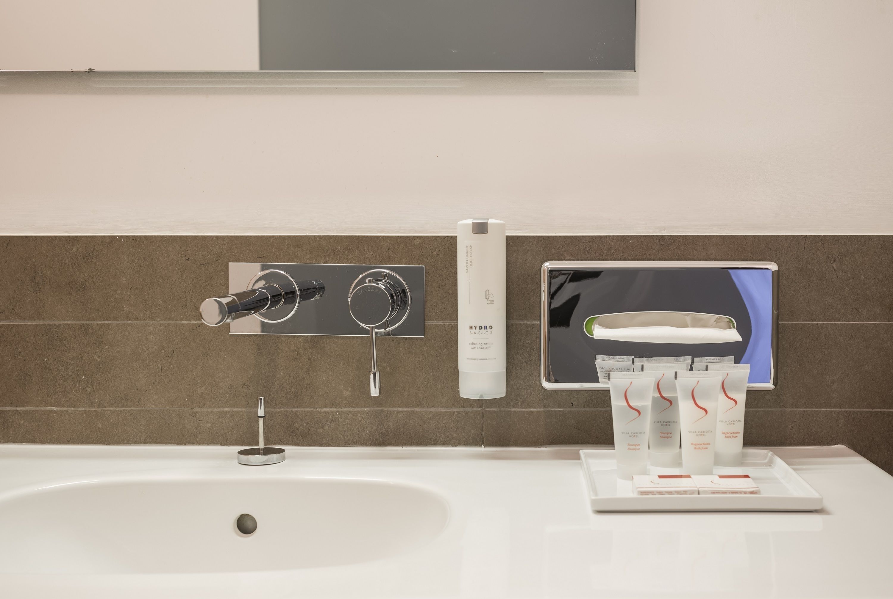 Un baño moderno con un lavamanos grande, un espejo y un dispensador de jabón en la pared.