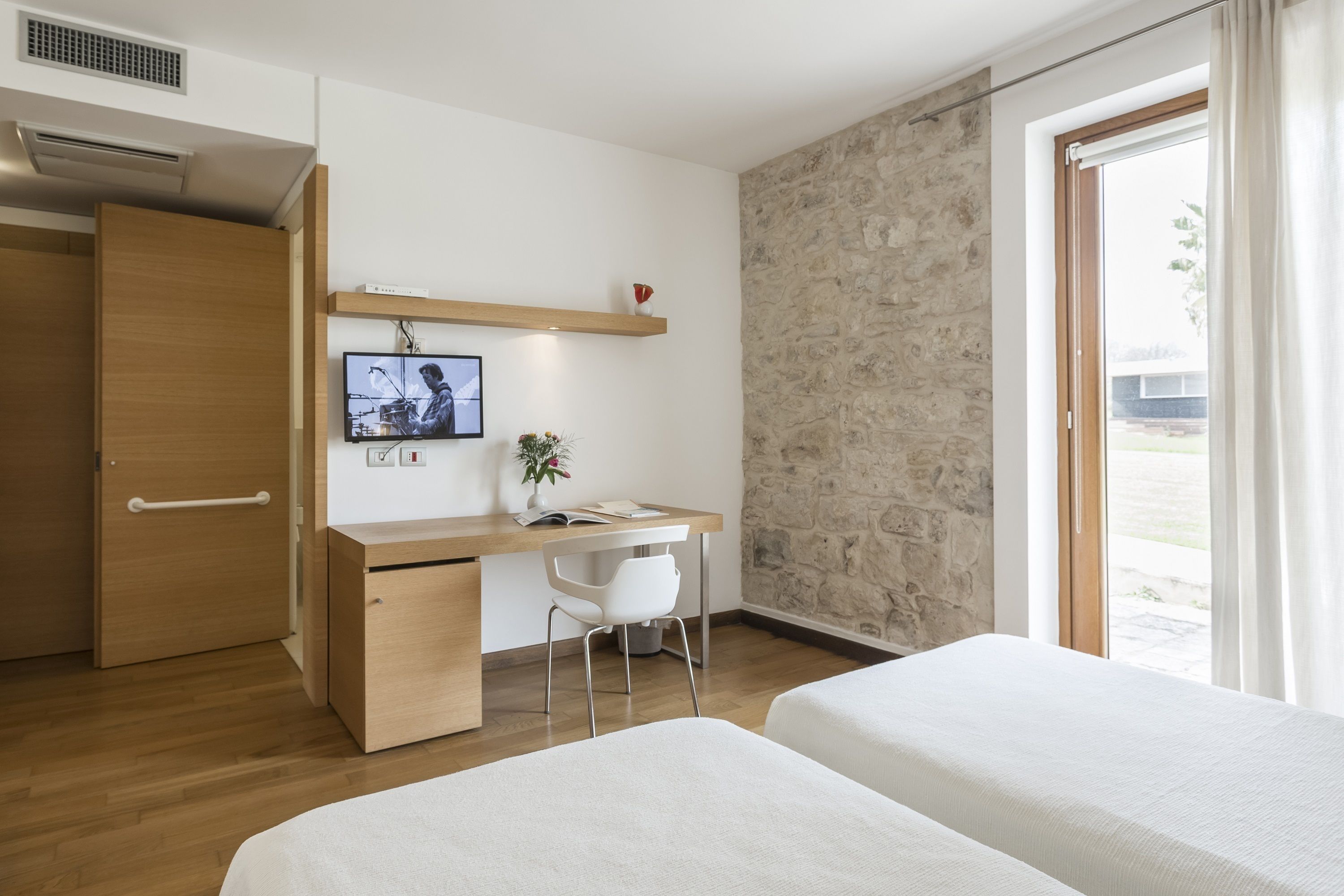 Une chambre avec un bureau en bois, une télévision, une chaise et deux lits.