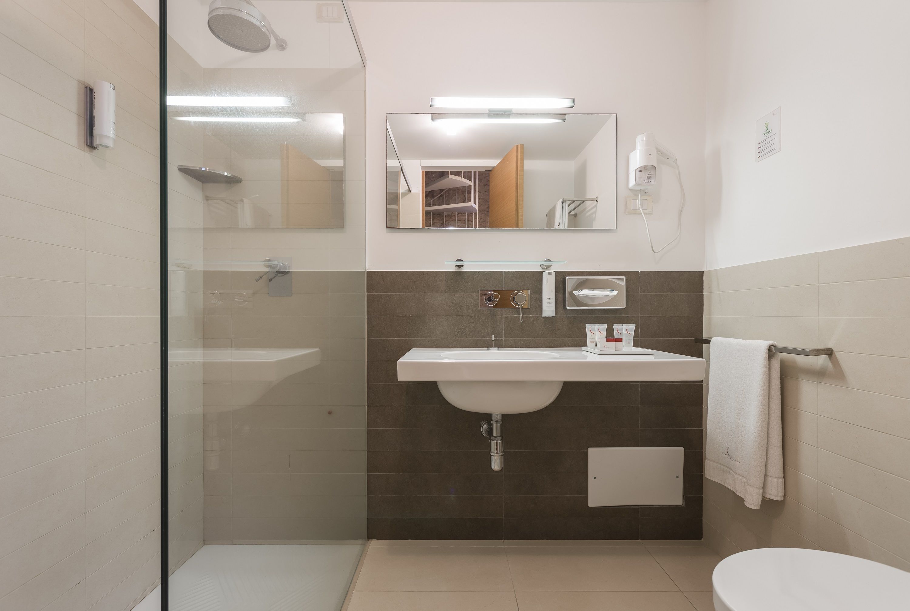 Une salle de bain moderne avec une douche à l’italienne en verre, un lavabo blanc avec un miroir au-dessus et un porte-serviettes fixé au mur.