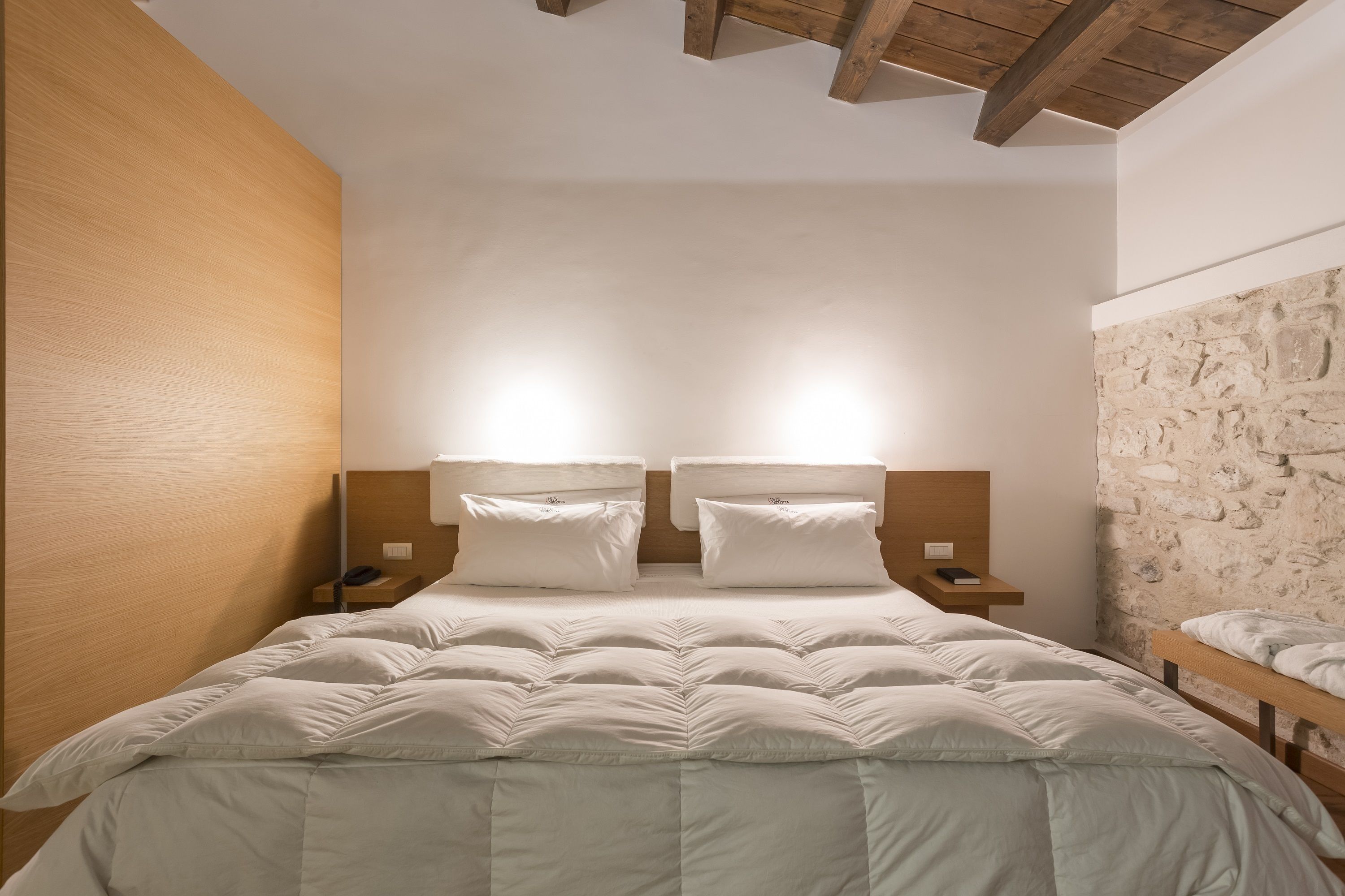 A bedroom with a large bed, two bedside tables, and a stone wall.
