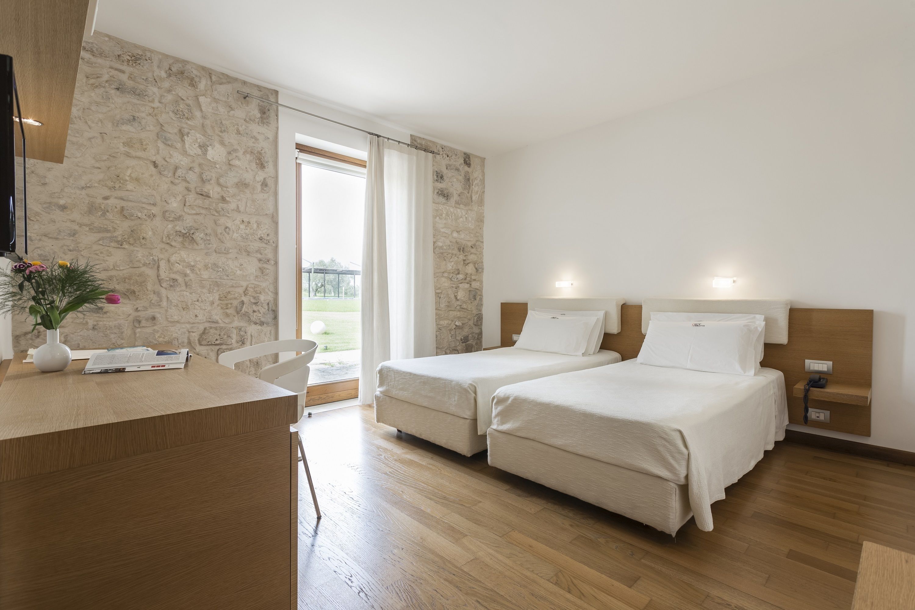 Une chambre d’hôtel avec deux lits, un bureau et un mur en pierre.