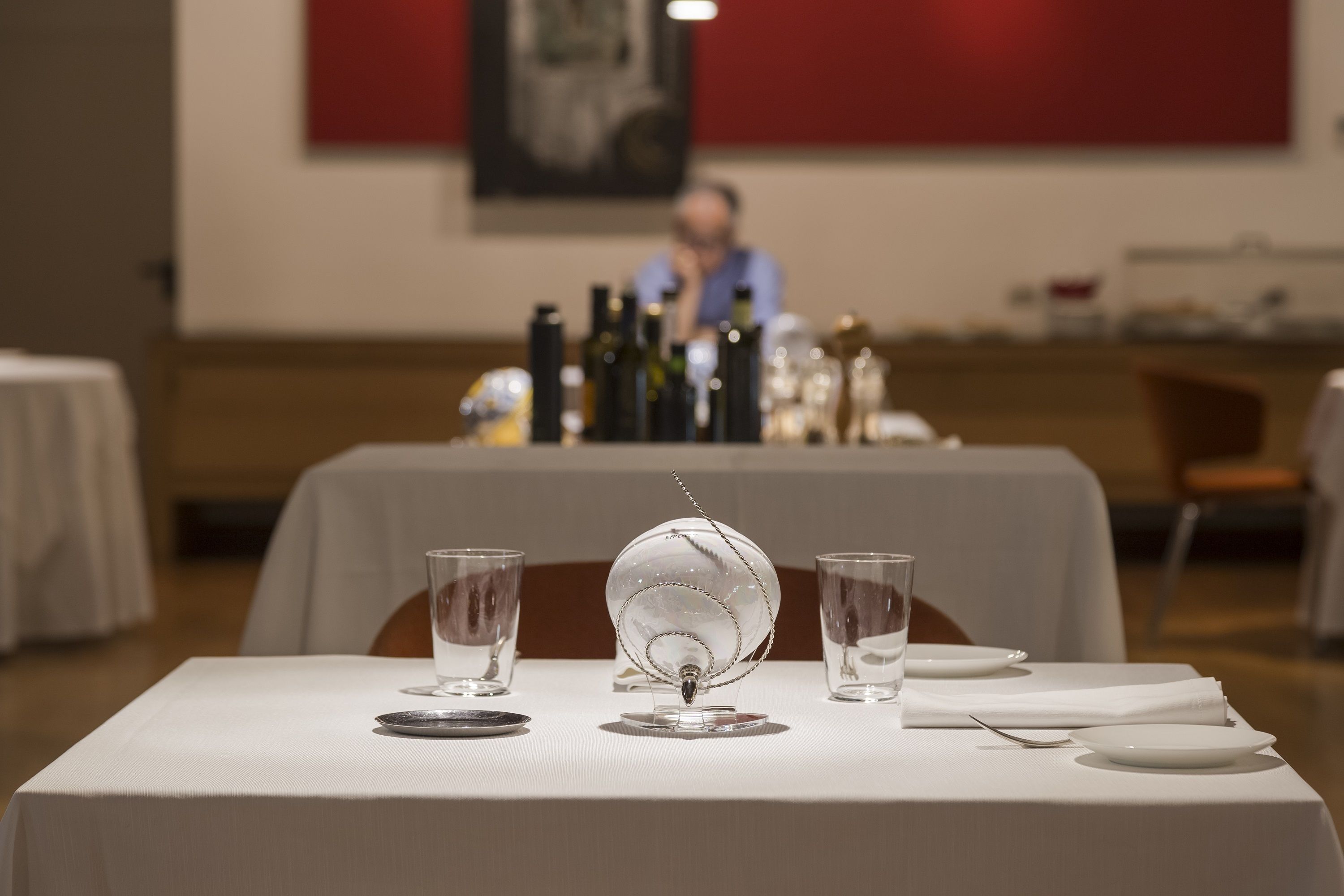 A dining table set with clear glassware, a decorative glass centerpiece, and a bottle of water.