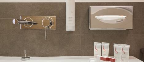 A modern bathroom with a white bathtub, a silver faucet, a handheld showerhead, and a set of toiletries on a tray.