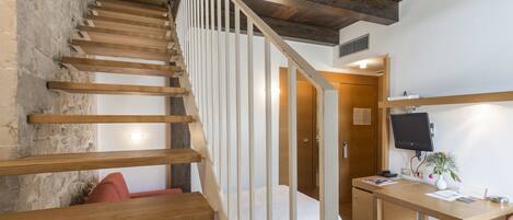 A staircase with wooden steps and white railings leading to a room with a desk, chair, and a television.
