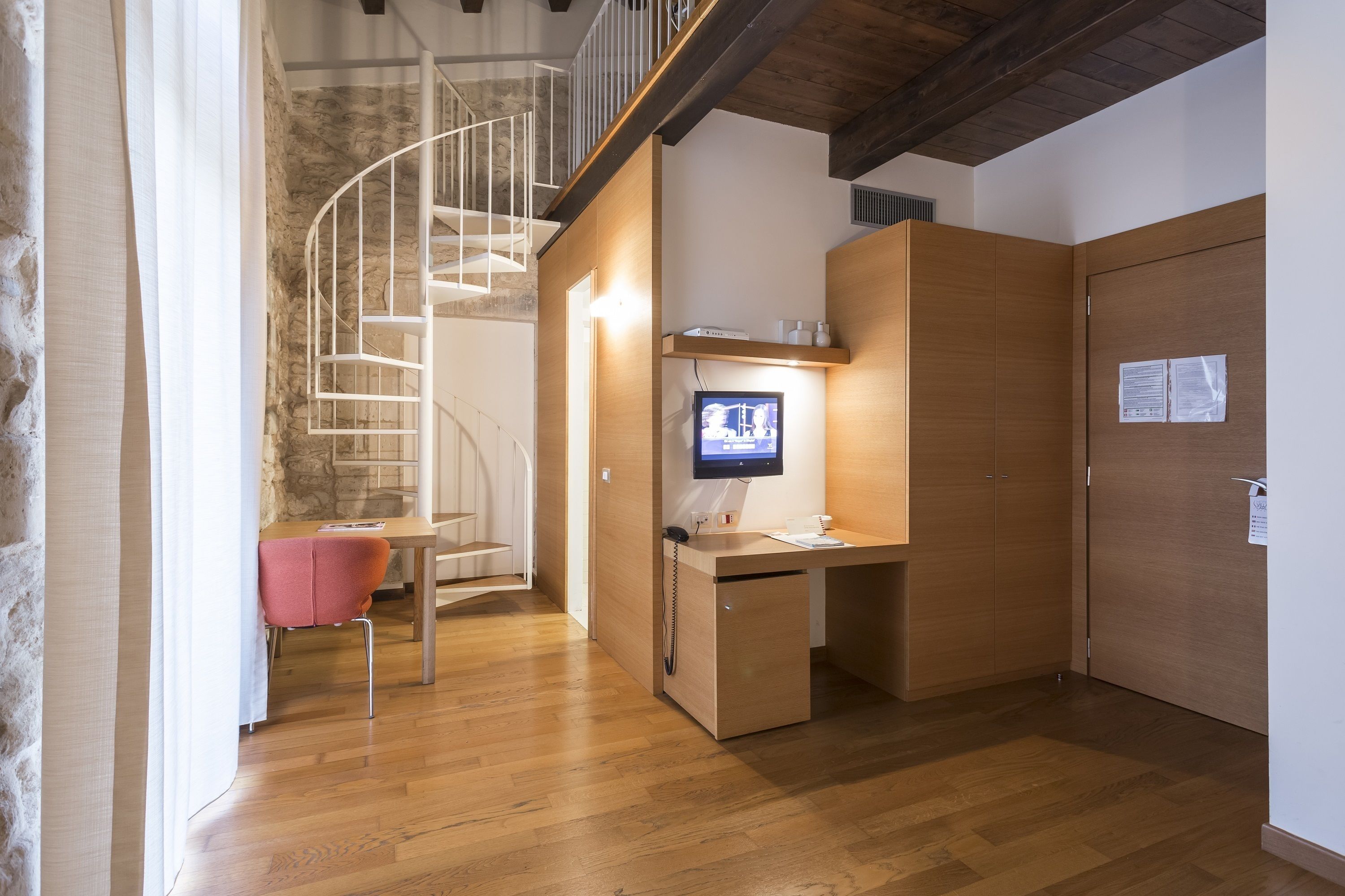 Un espace de bureau moderne avec un bureau en bois, un écran d’ordinateur, un téléphone et un escalier en colimaçon.
