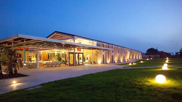 Un edificio moderno con un área exterior cubierta, posiblemente un restaurante o cafetería, con una entrada bien iluminada y un césped en primer plano.