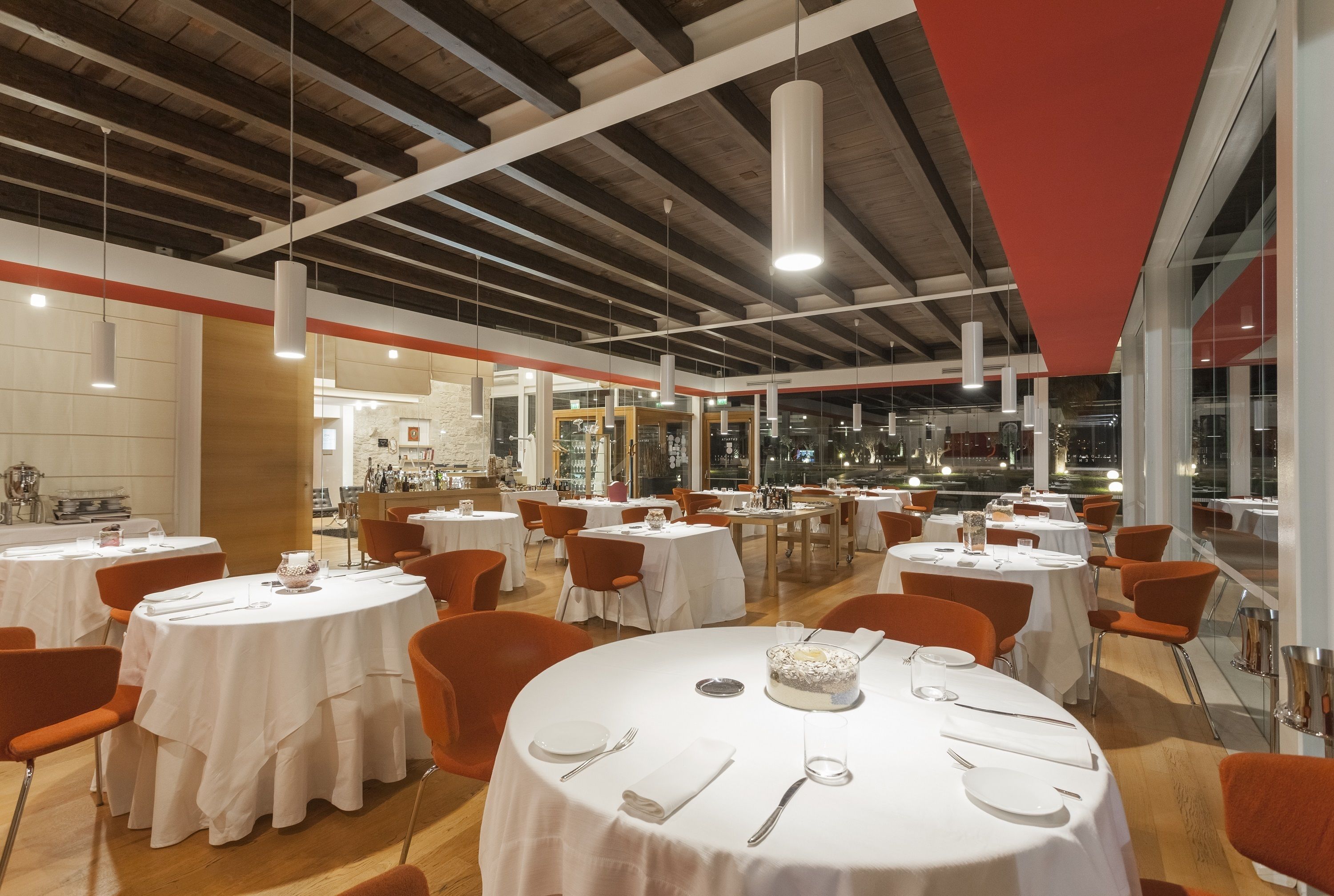 Un comedor amplio con mesas redondas, sillas naranjas y un pastel grande como pieza central.