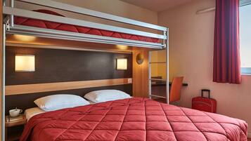 Un lit superposé avec une couverture matelassée rouge, des lampes de chevet et une valise dans une chambre d’hôtel.