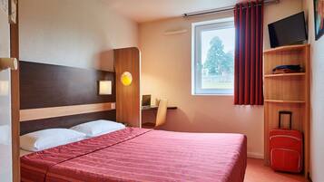 A hotel room with a bed, a desk, a chair, a TV, and a suitcase.
